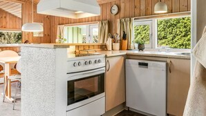 Una cocina con paredes de madera, estufa, lavavajillas y ventana con vista a la vegetación.
