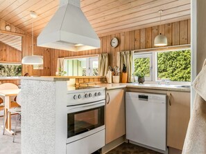 A kitchen with wooden walls, a stove, a dishwasher, and a window with a view of greenery. - "Jürgen" - 2.5km from the sea by Interhome (Blokhus)