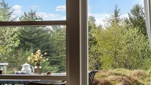 Vista desde una ventana con jardín, árboles, una mesa, una silla y un florero.