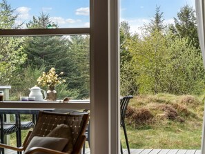 A view from a window overlooking a garden with trees and a table with a chair and a vase of flowers. - "Jürgen" - 2.5km from the sea by Interhome (Blokhus)