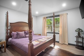 Ein Bett mit Baldachin, ein hölzerner Kopfteil, ein Nachttisch, eine Lampe und ein Fenster mit Vorhängen.