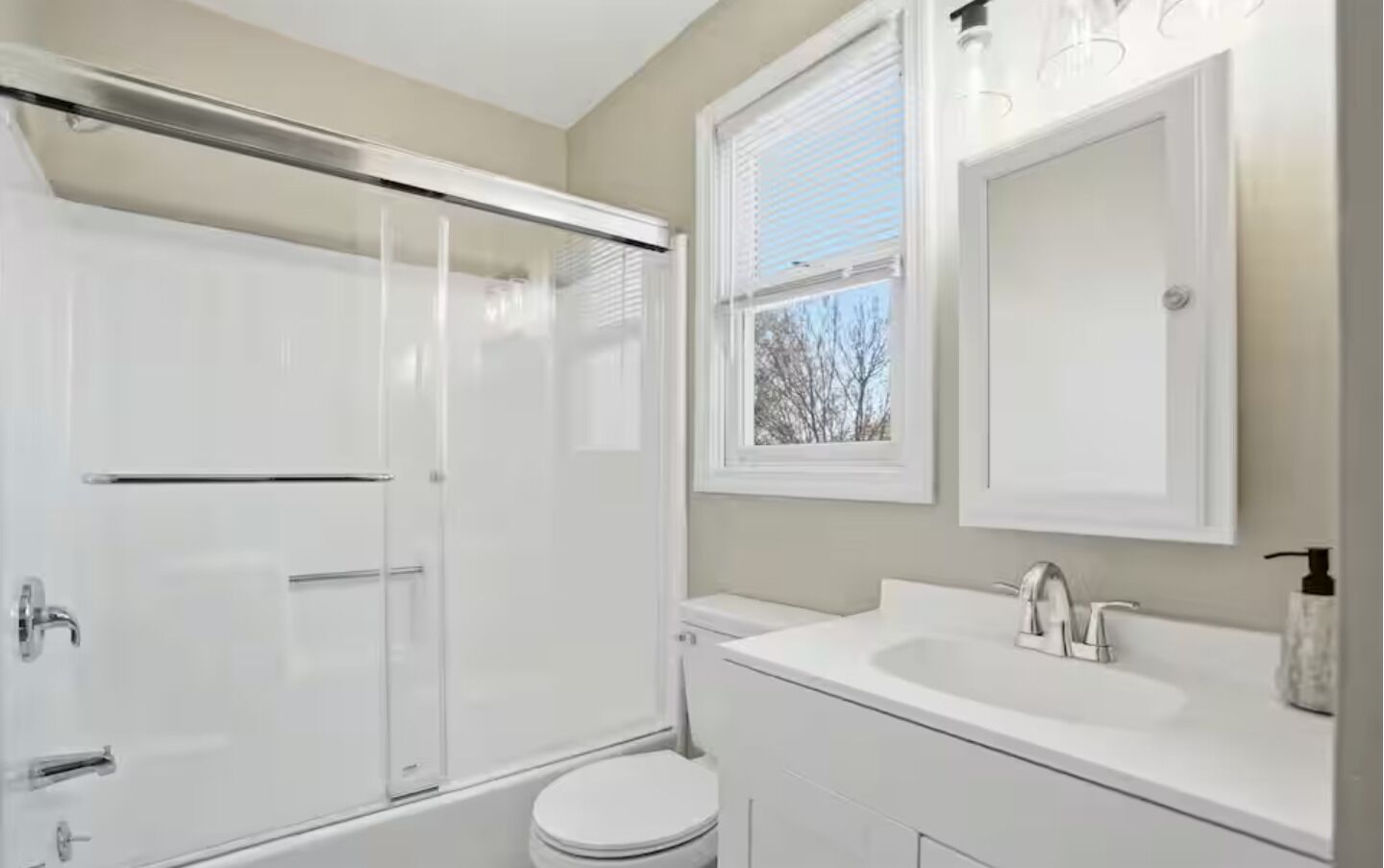 Un baño con cabina de ducha de vidrio, inodoro, lavamanos con espejo y ventana.