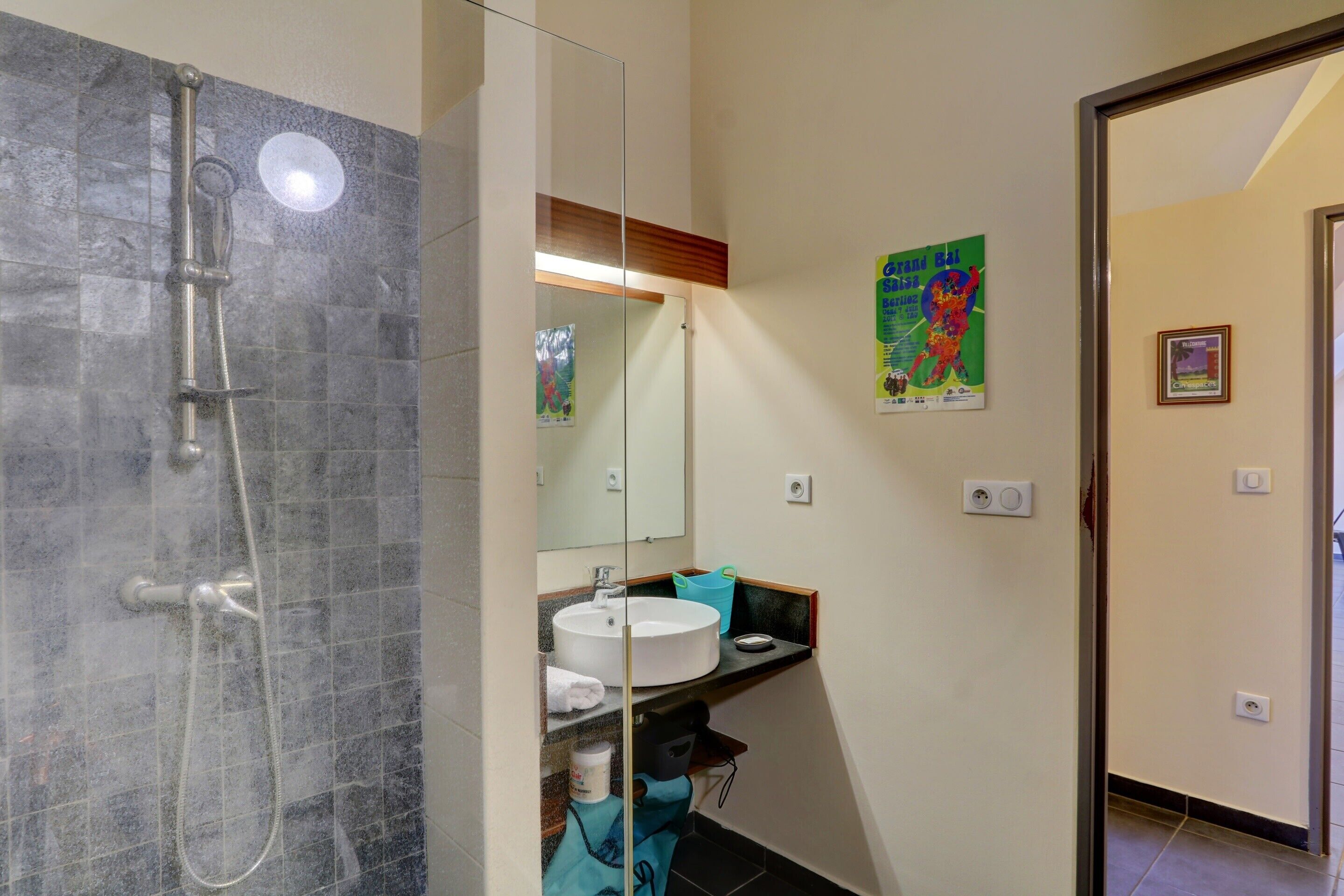 A bathroom with a glass shower enclosure, a sink, and a mirror.