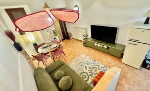 A compact living space with a sofa, dining table, chairs, a television, and a refrigerator. - Pink House - InBorgo (ACQUASPARTA)