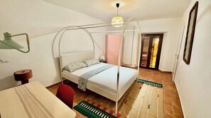 A bedroom with a bed, a desk, a chair, a lamp, a radiator, and a door leading to another room. - Pink House - InBorgo (ACQUASPARTA)