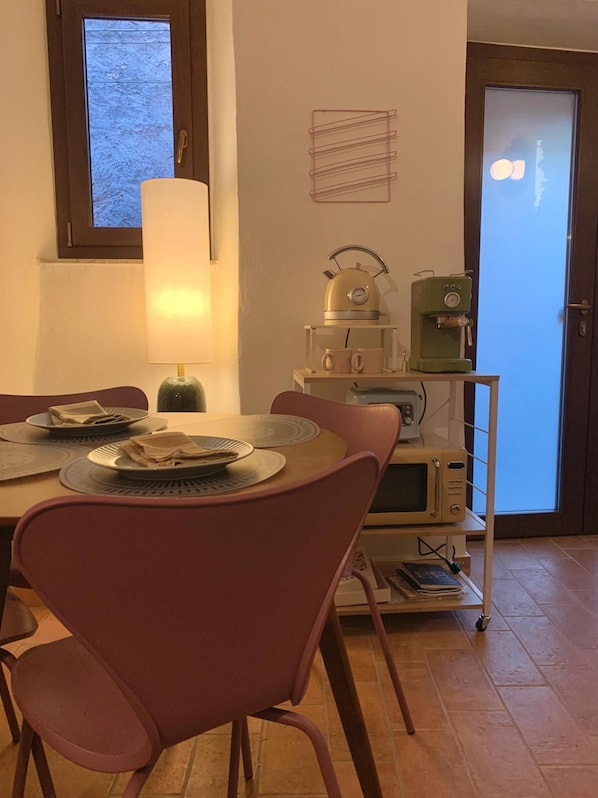 A dining area with a table set for two, a lamp, a kettle, a coffee maker, and a microwave.