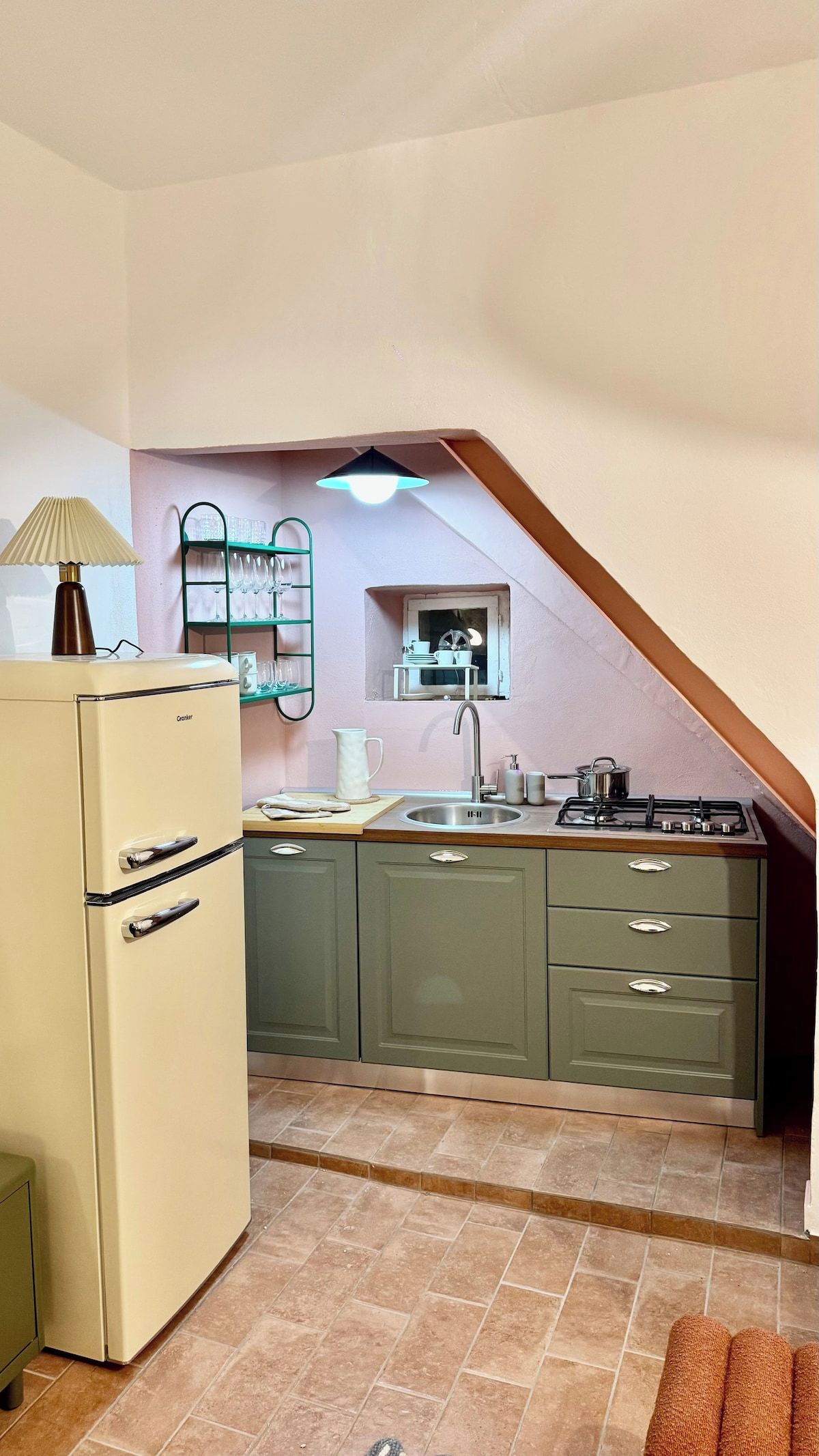 A compact kitchen with a refrigerator, sink, and stove, featuring a small window and a tiled floor.