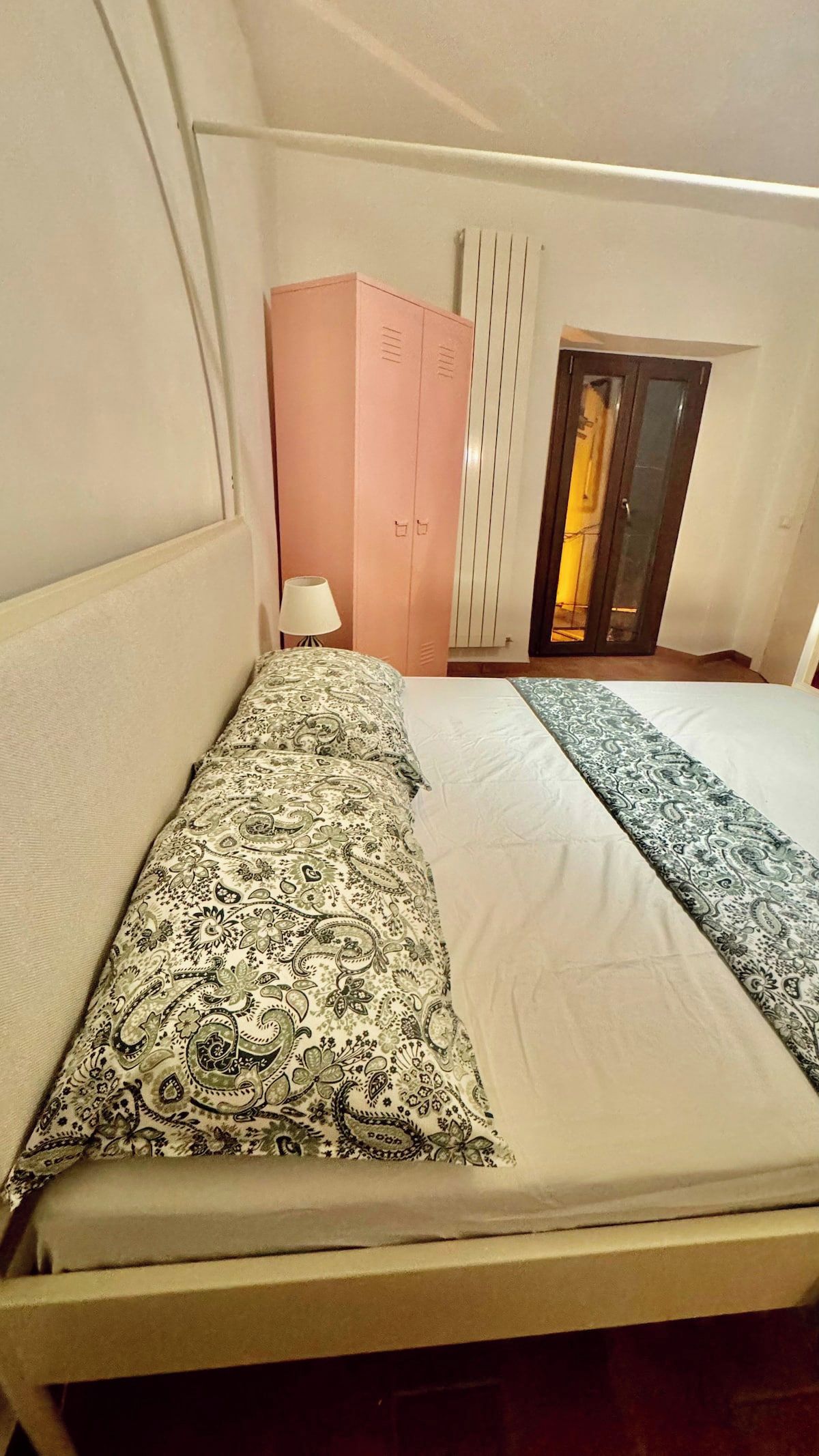 Una stanza con un letto, un armadio, una lampada e un termosifone.