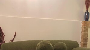 En grøn sofa med to runde puder, en brun skammel og en tæppe med et mønster.