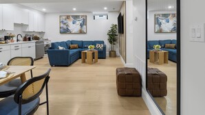 Una sala de estar moderna con un sofá azul, una mesa de comedor con sillas y un espejo grande que refleja la habitación.