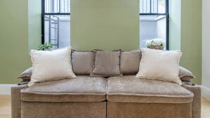 Un sofá seccional marrón con tres cojines en una habitación con paredes verdes y una ventana.
