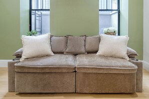 Ein braunes Ecksofa mit drei Kissen in einem Zimmer mit grünen Wänden und einem Fenster.