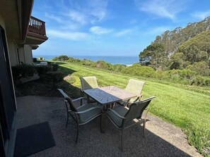 An outdoor patio with a table and chairs, overlooking a well-maintained lawn and a view of the ocean. - Accessible North Bluff Open Floorplan-Ocean View (Aptos)
