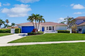 A residential house with a blue garage, a well-maintained lawn, and a clear sky. - Marco Island Oasis, Private Pool, Waterfront & Family Fun! (Marco Island)