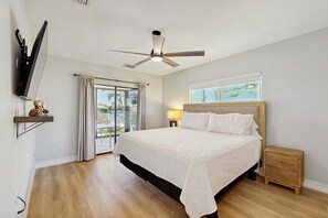 A bedroom with a bed, a ceiling fan, a TV mounted on the wall, a window with a view, and a nightstand. - Marco Island Oasis, Private Pool, Waterfront & Family Fun! (Marco Island)
