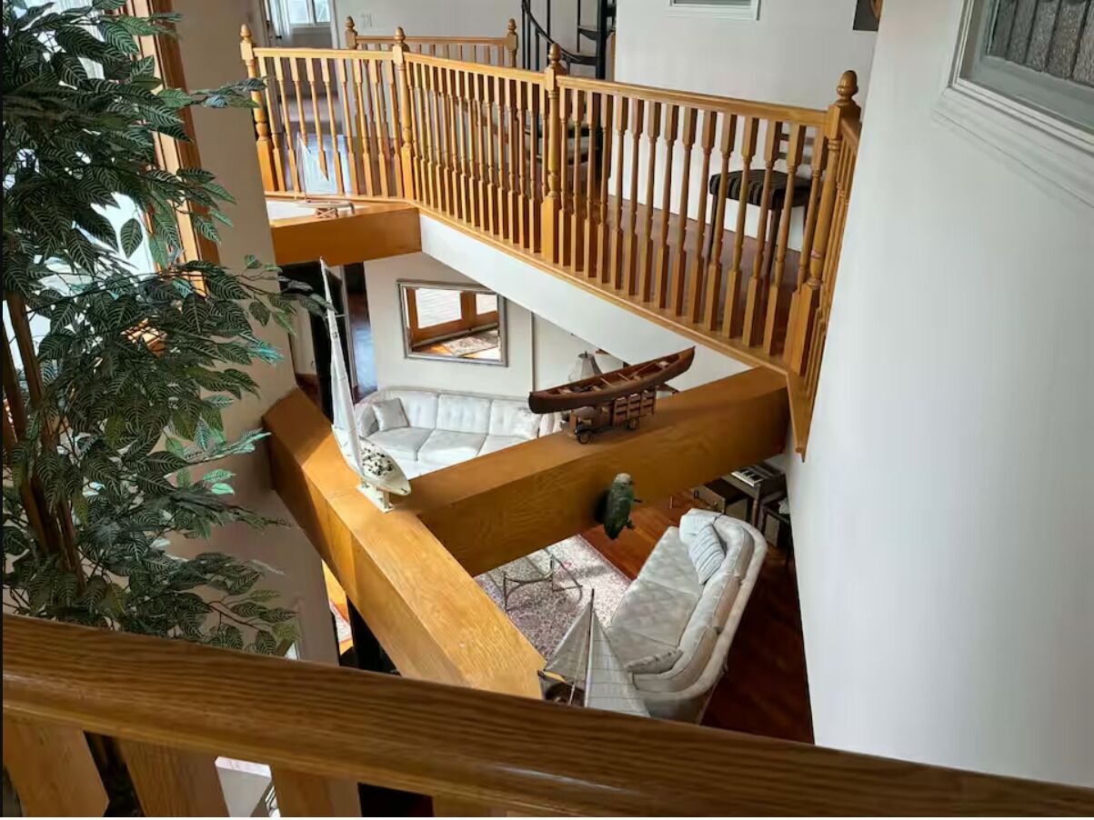 Ein mehrgeschossiges Interieur mit einer Holztreppe, einem Sofa, einem kleinen Tisch und einem dekorativen Schiffsmodell.