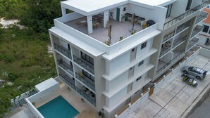 Ein mehrstöckiges Gebäude mit Dachterrasse, Pool und Parkplatz.