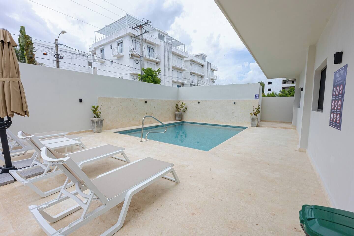 Ein Swimmingpool mit Liegestühlen, eine kleine Poolterrasse und ein Gebäude im Hintergrund.