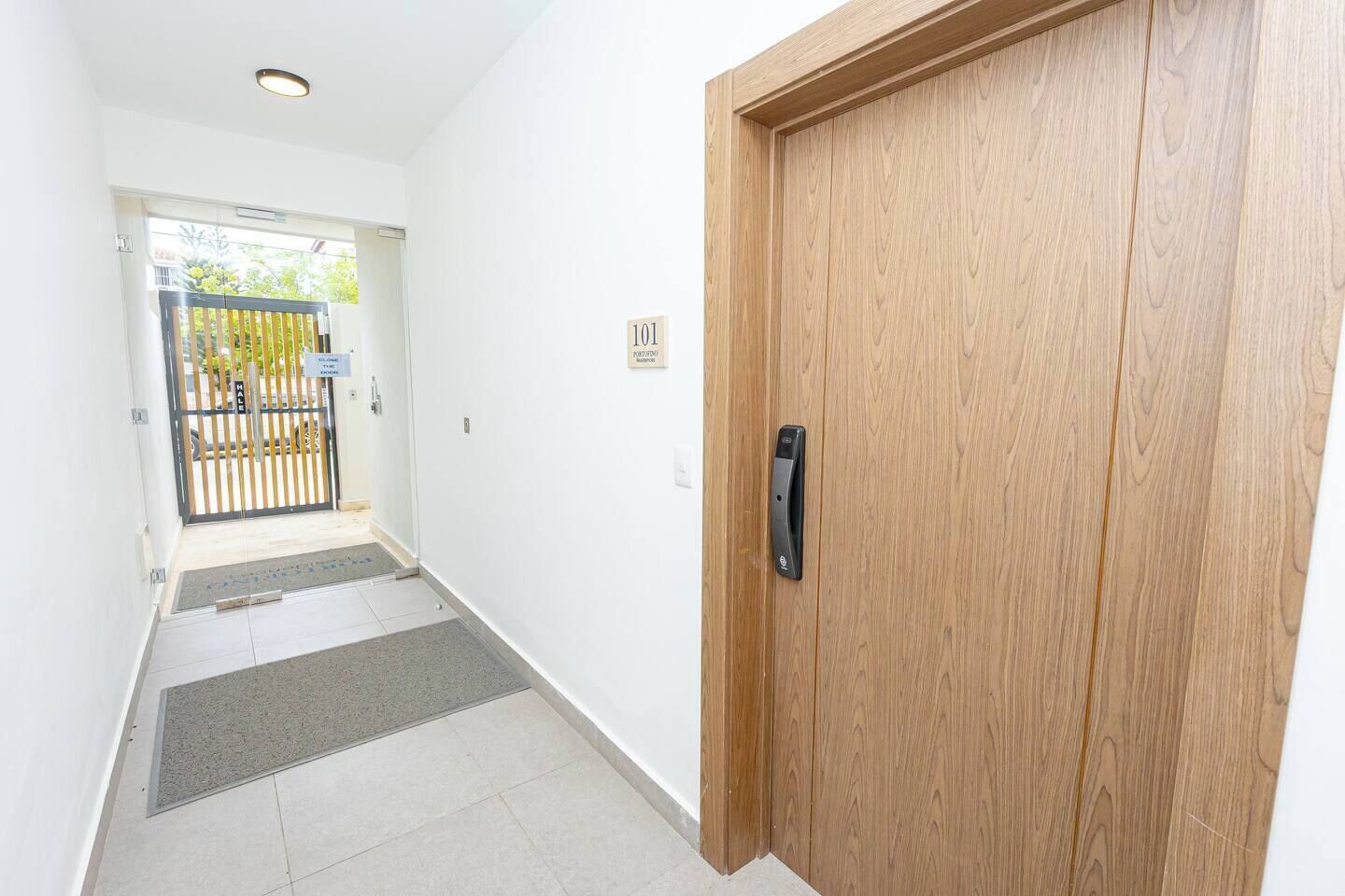 A hallway with a wooden door, a tiled floor, and a gate leading outside.