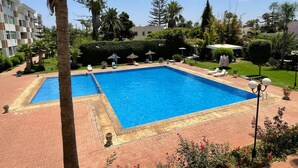 A rectangular swimming pool with a tiled deck, surrounded by palm trees and greenery.