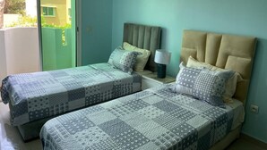 A bedroom with two beds, a nightstand, a lamp, and a sliding glass door leading to an outdoor area.