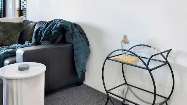 Uma sala de estar moderna com um sofá, uma mesinha redonda branca e uma mesa de centro de vidro com um livro e uma garrafa.