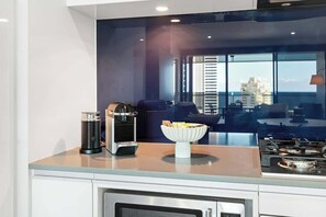 A modern kitchen with a built-in stove, a coffee machine, and a bowl of bread on the counter. - Steps to Cavill Ave | Ocean View 2BR | 3 Pools (Surfers Paradise)