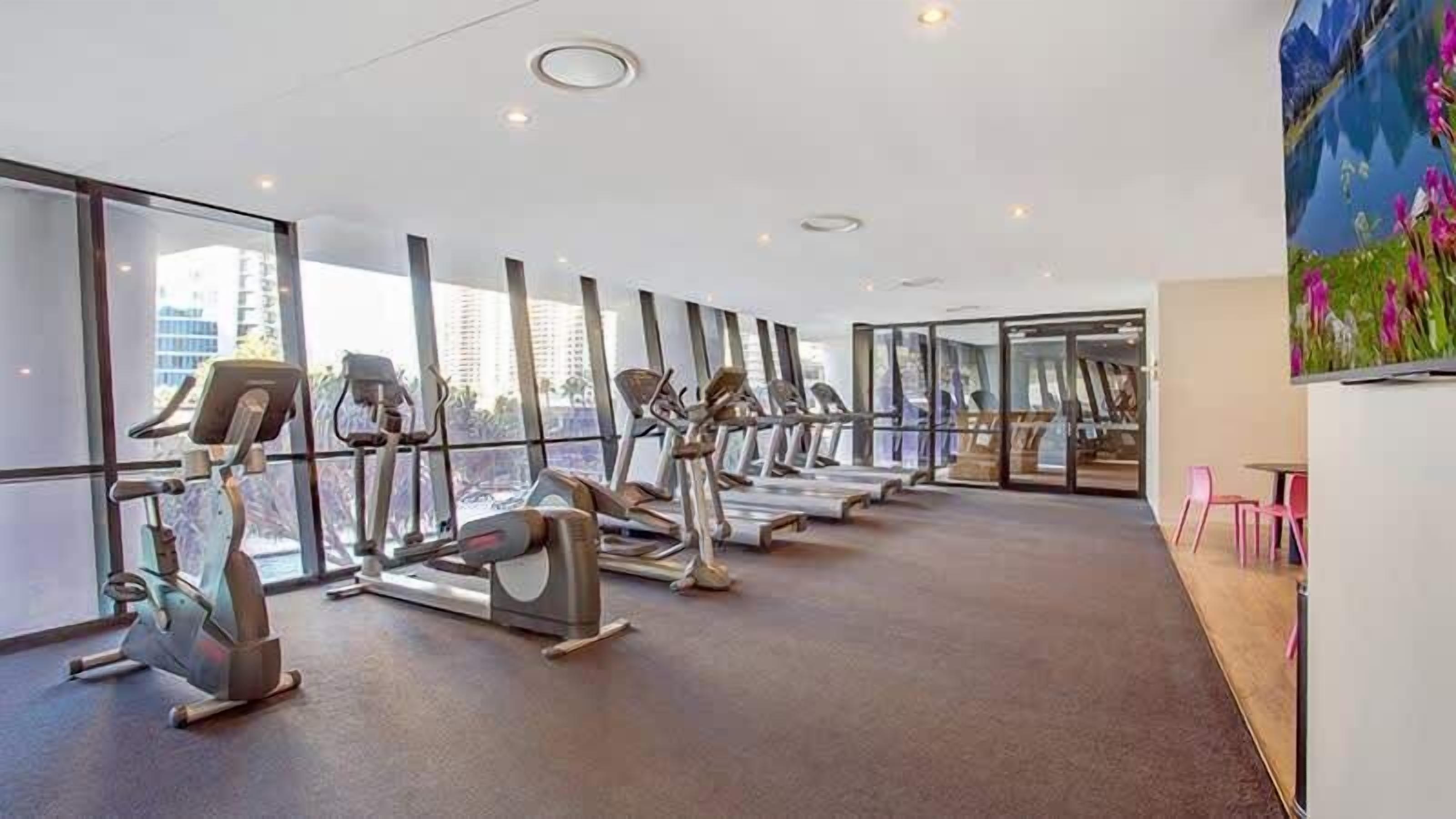Een sportschool met cardioapparatuur, grote ramen en stadszicht.