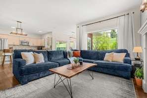 A modern living room with a sectional sofa, a wooden coffee table, and a view of the kitchen and outdoors.