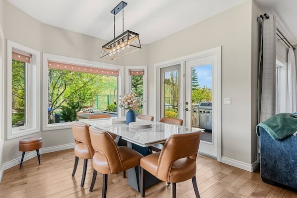 A dining area with a table and chairs, large windows, and a view of the outdoors.
