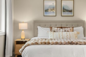 A bedroom with a bed, a nightstand with a lamp, and two framed pictures on the wall.