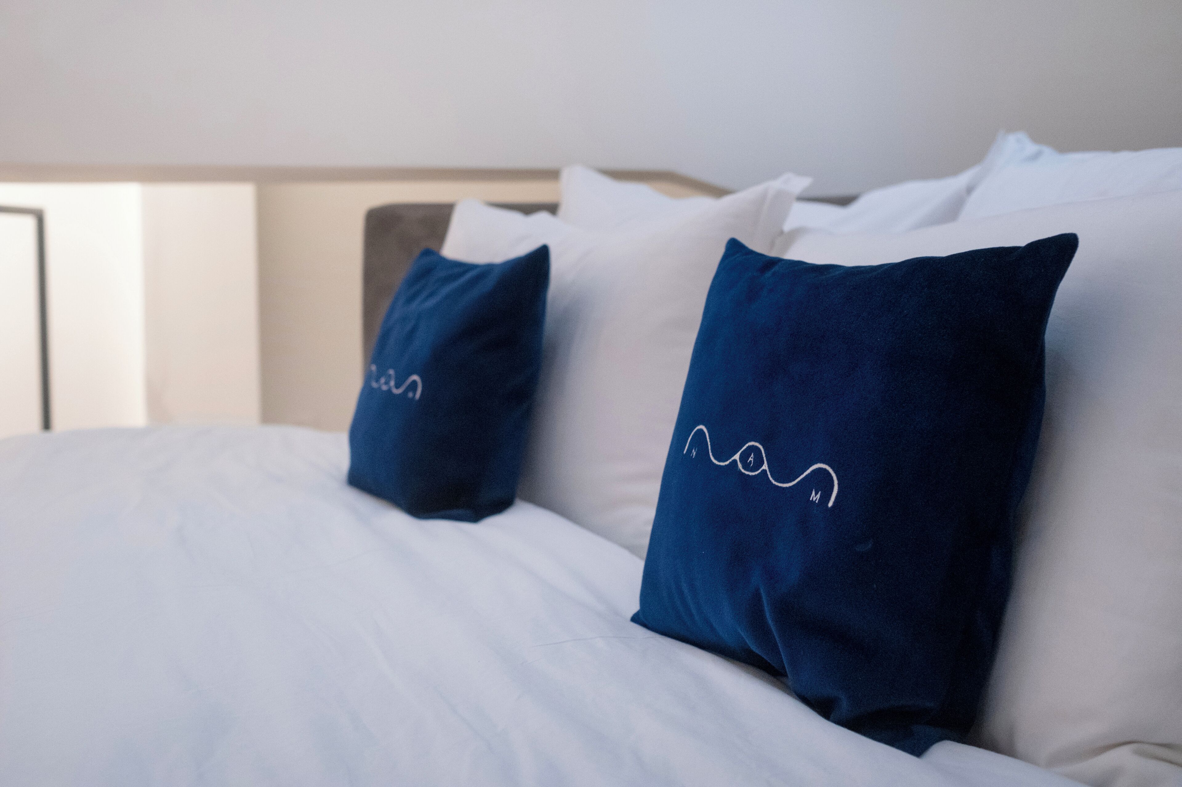 A bed with white bedding and two dark blue pillows with a white line design.