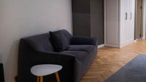 A modern living room with a dark sofa, a small white table, and a wardrobe. - NAM HOTEL (Prizren)