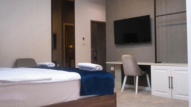 A hotel room with a bed, a desk, a chair, a television, and a wardrobe. - NAM HOTEL (Prizren)