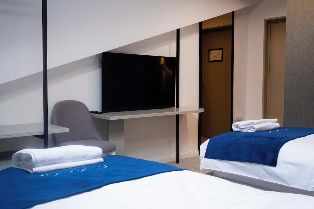 Habitación de hotel con dos camas, un televisor montado en la pared, un escritorio y una silla.