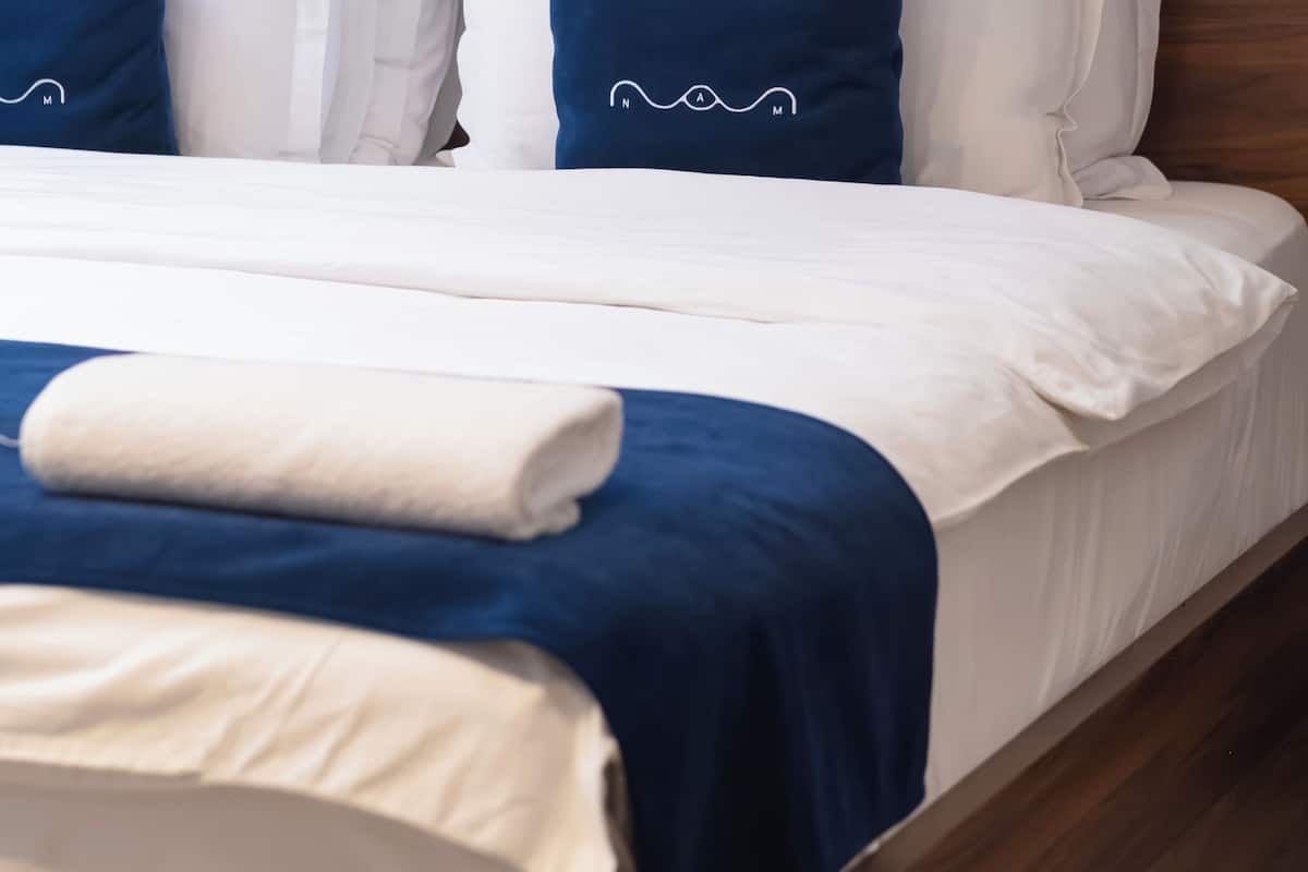 Una cama bien hecha con ropa de cama blanca y azul, un cabecero de madera y una almohada azul con un diseño blanco.