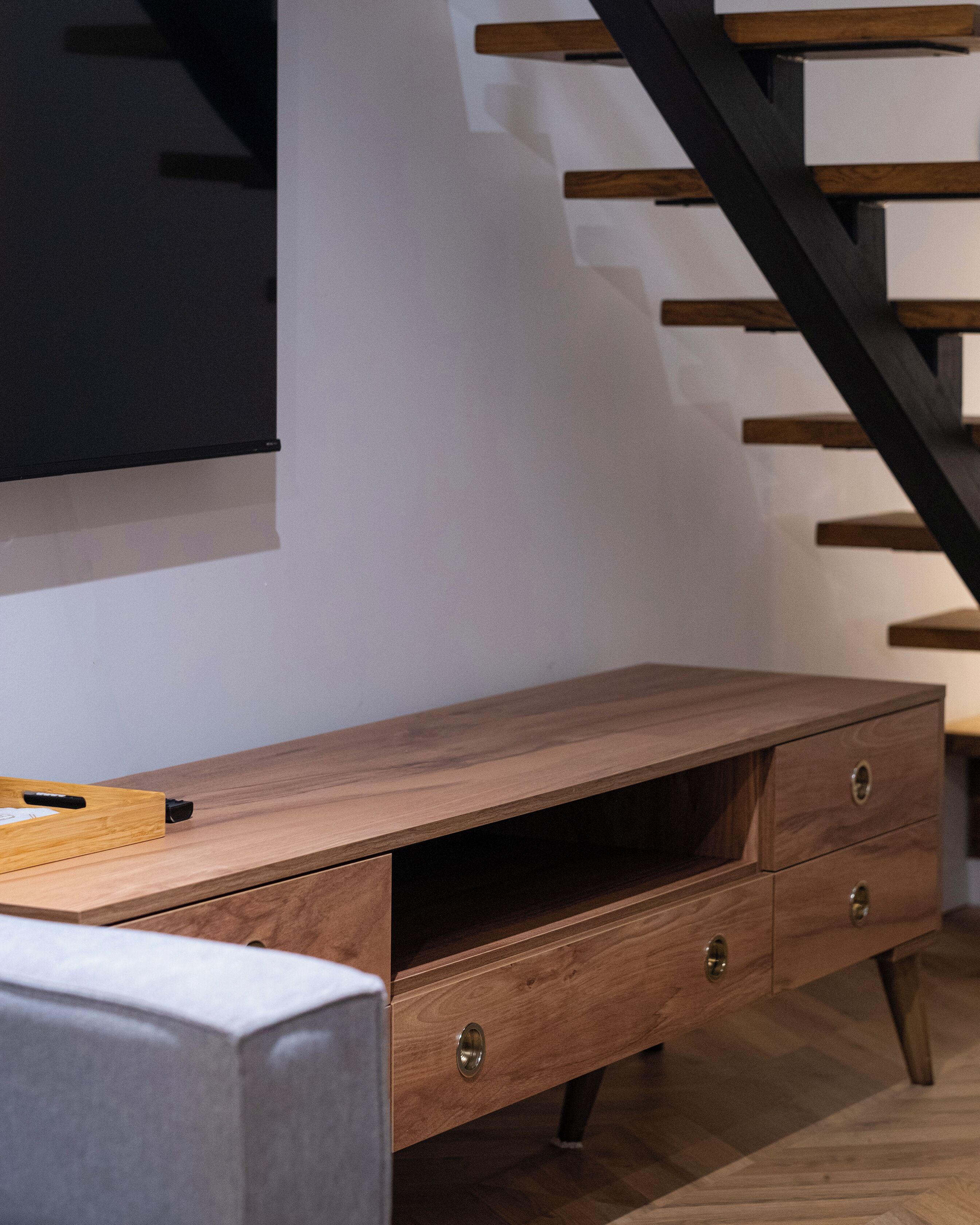 A modern room with a wooden desk, a flat-screen TV mounted on the wall, and a staircase with wooden steps.