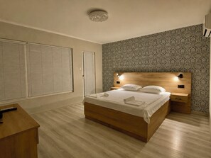 A bedroom with a wooden bed, two bedside tables, a nightstand, a desk, and a patterned wallpaper.