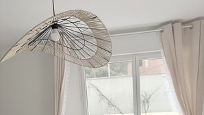 Ett sovrum med en säng, ett fönster med gardiner, en hängande lampa och utsikt över omgivningen.