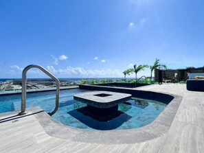 Ein Pool mit einer Steinstruktur in der Mitte, umgeben von einer Terrasse mit Metallgeländer.