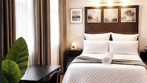Une chambre d’hôtel comprenant un lit, un bureau, une chaise, une plante en pot et une table de chevet avec une lampe.