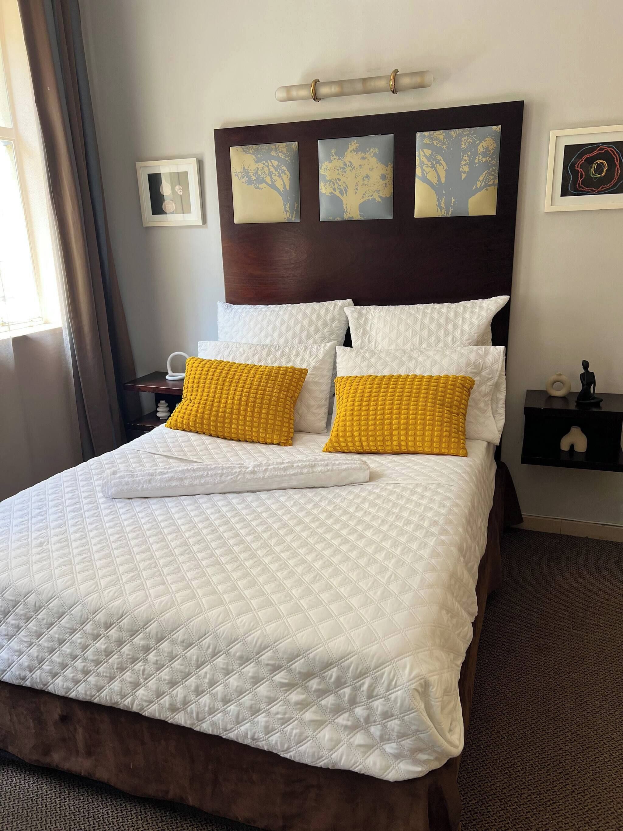 Habitación de hotel con cama, mesita de noche y lámpara de pared.