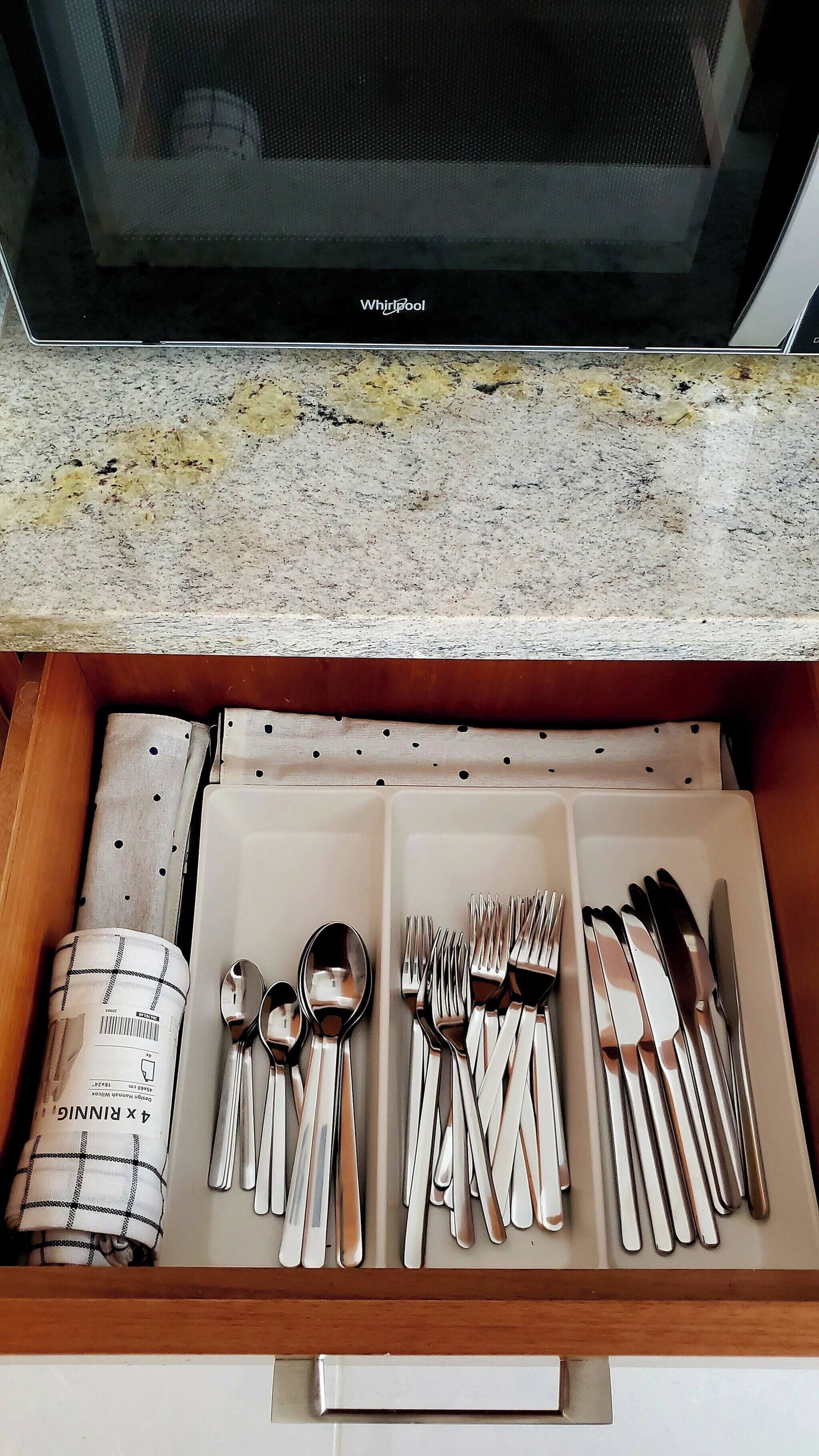 Un cajón con cubiertos ordenados, incluyendo cucharas, tenedores y cuchillos, y un salvamanteles enrollado.