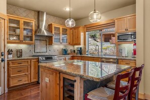 A kitchen with wooden cabinets, a stainless steel range hood, a granite countertop, and a large island with chairs. - Ski Slope Views Tahoe Donner Retreat (Truckee)