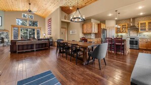 Une cuisine spacieuse avec des meubles en bois, un coin repas doté d’une grande table et de chaises, et un plafond avec des poutres apparentes.