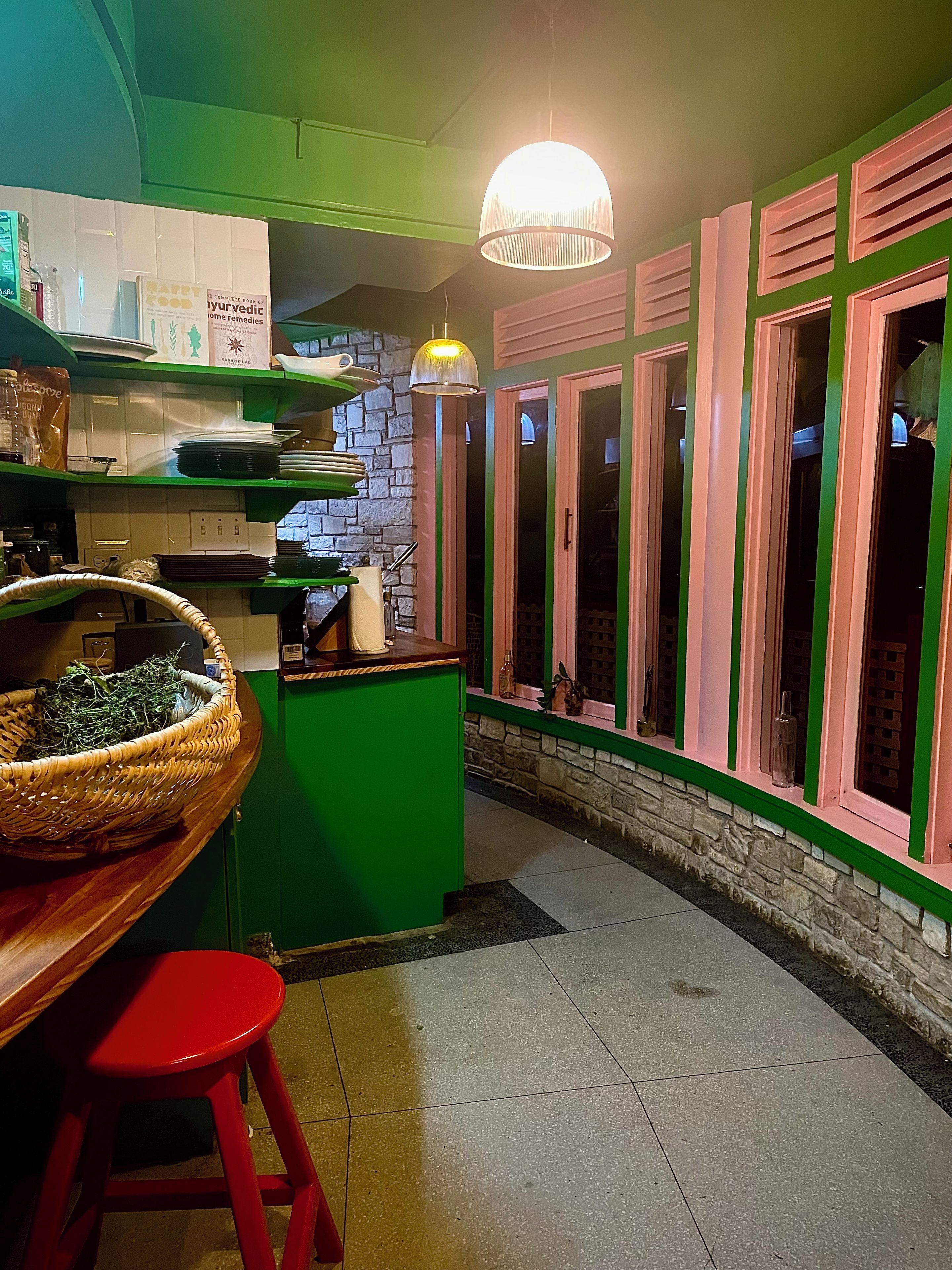 A kitchen with green cabinets, a red stool, and a hanging light fixture.