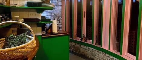 A kitchen with green cabinets, a red stool, and a hanging light fixture.