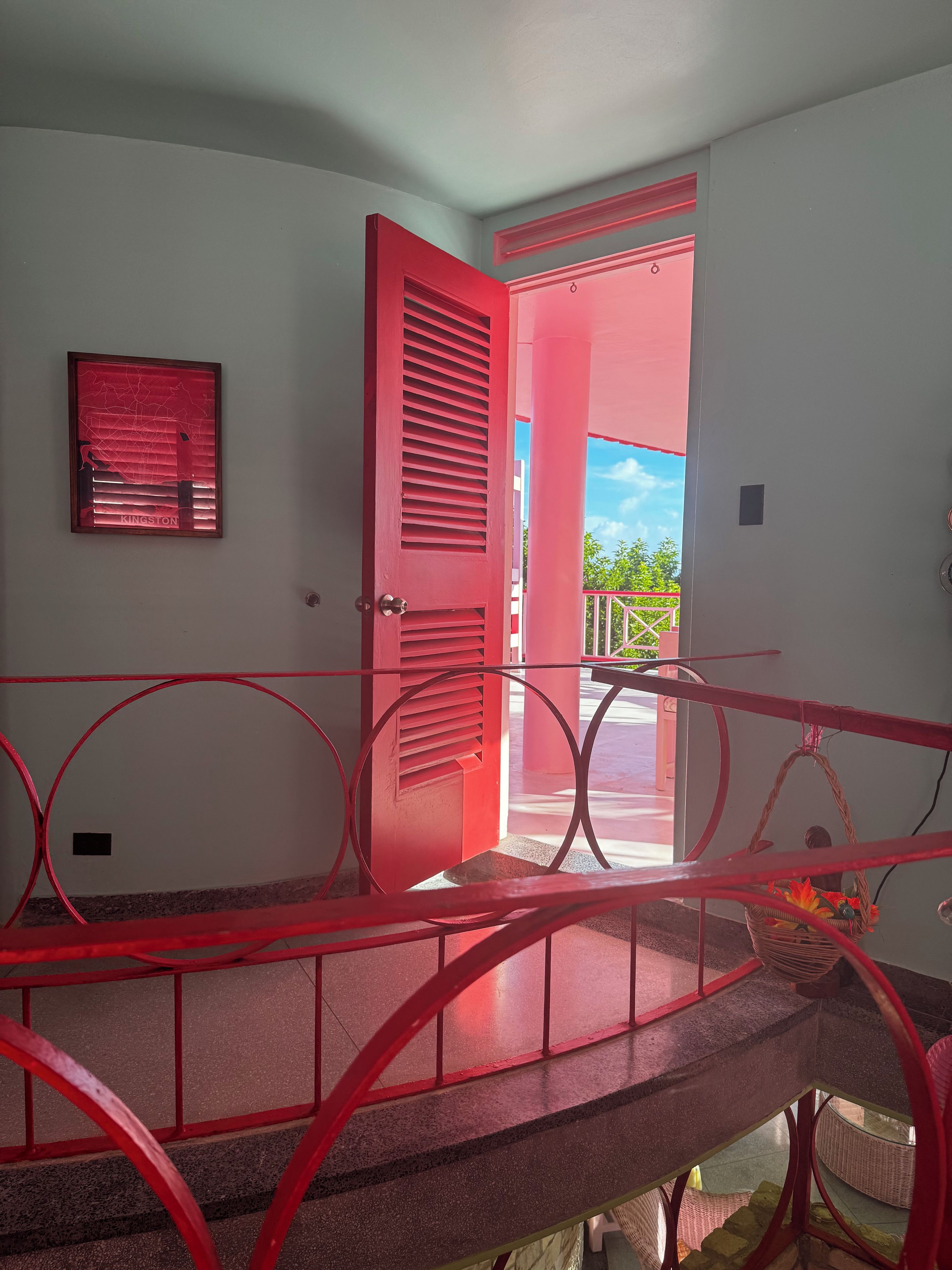 A red-framed door leading to an outdoor area with a view of greenery and a clear sky.