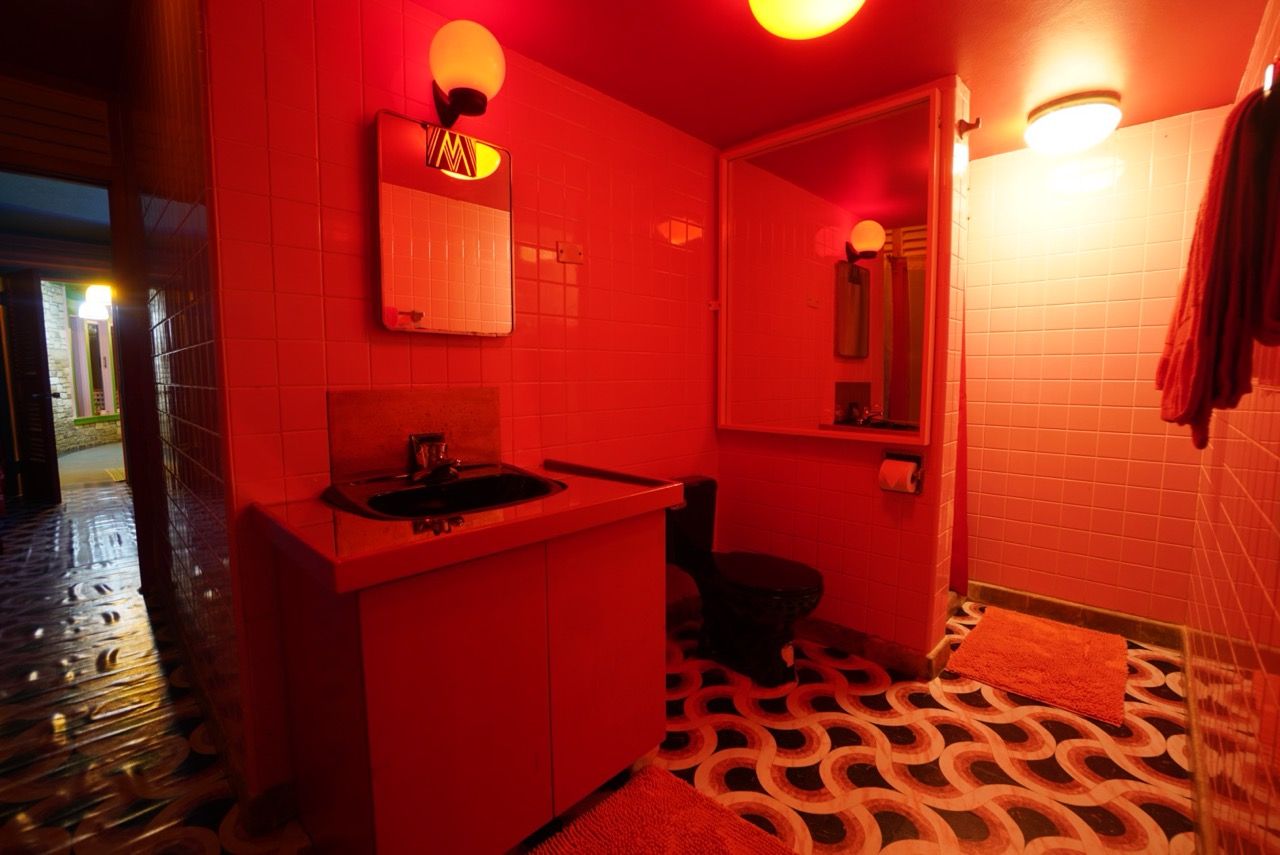 Een badkamer met een rood kleurenschema, een wastafel, een spiegel en een vloer met een patroon.