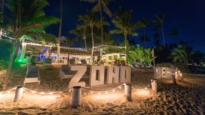 A beachside resort with lounge chairs, palm trees, and string lights. - Cozy 2BR/2Bth walk 2 the beach. Pool view & Wi-Fi (Punta Cana)